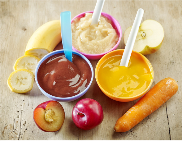 A group of fruits and vegetables slices on a wooden surface with three bowls of pureed foods with a spoon sticking out.