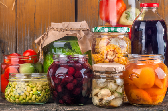 Fruits and vegetables in canning jars on a wooden surface with a wooden background.
