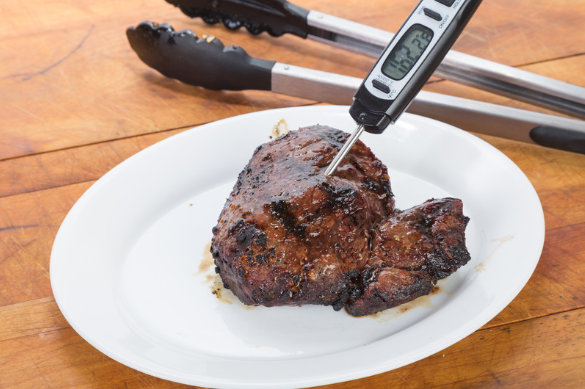 A digital food thermometer inserted into a steak registering 162.2 degrees Fahrenheit